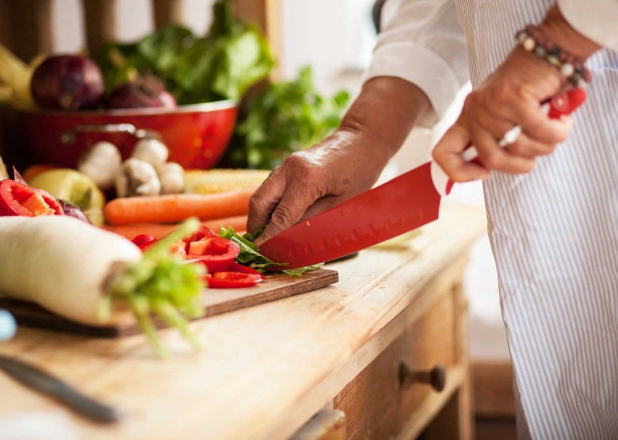 A person cutting vegetables on top of a wooden table.